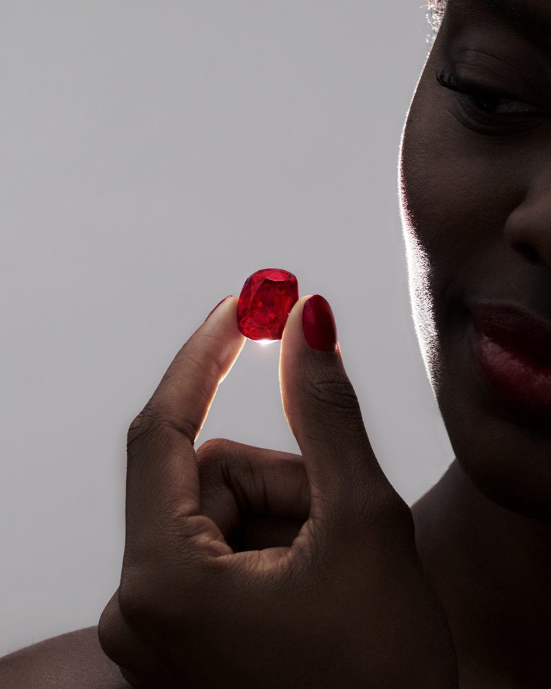 A woman holding a cushion-cut ruby up to the light